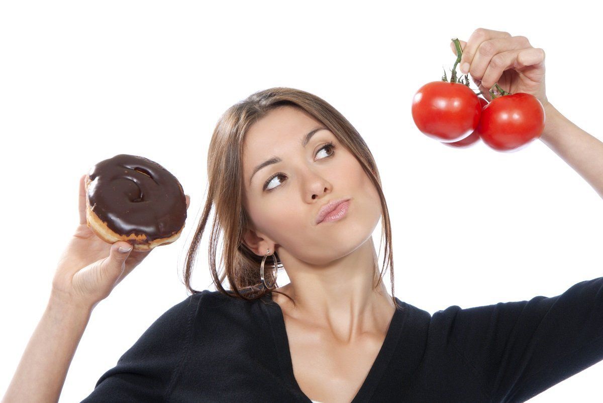 Healthy eating food concept. Woman comparing unhealthy donut and organic red tomatoes, thinking isolated on a white background