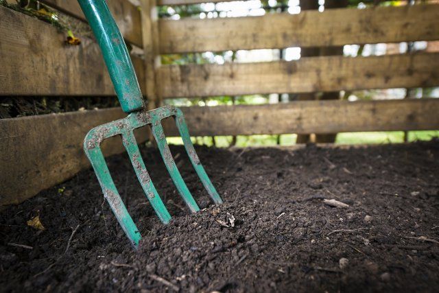 Garden fork turning black composted soil in wooden compost bin